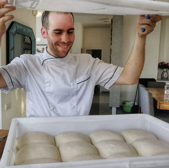 Alon in chef's whites lifting the lid off a tray of proofed dough balls